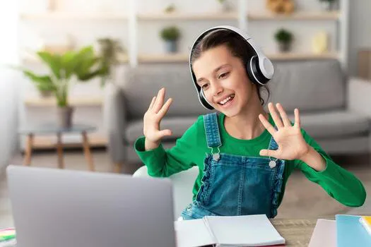 distance-education-portrait-of-smiling-schoolgirl-making-call-with-teacher-and-classmates-using-pc-cheerful-student-in-wireless-headphones-talking-and-waving-both-hands-showing-ten-10-fingers-photo